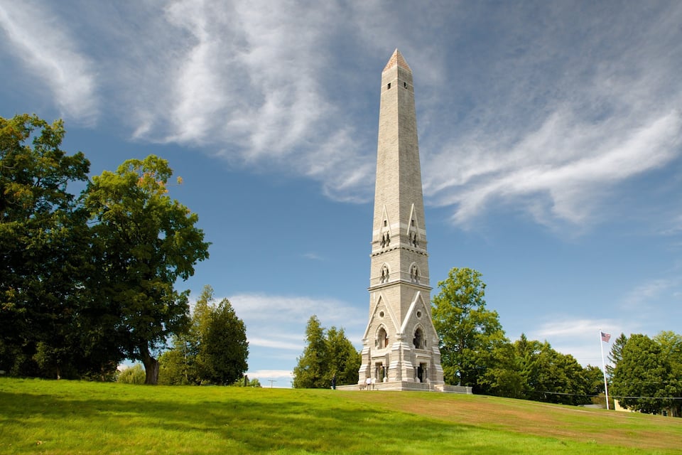 The Washington Monument surrounded by lush green trees and grass under a partly cloudy sky.