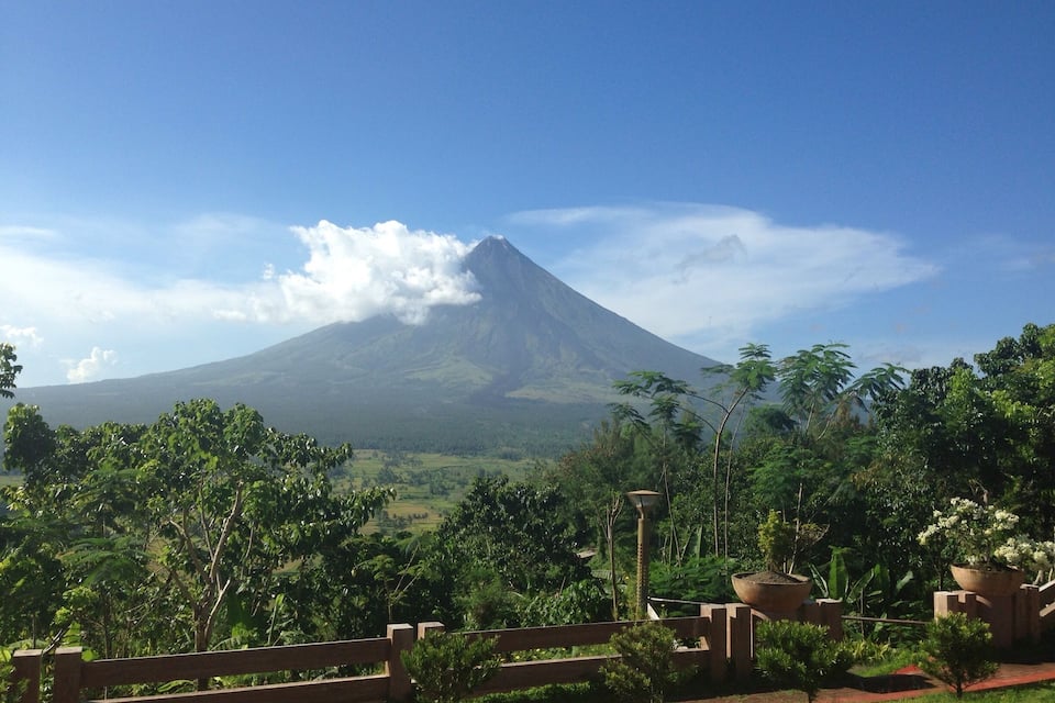 A mountain with a cloud base, surrounded by lush greenery and a wooden fence.
