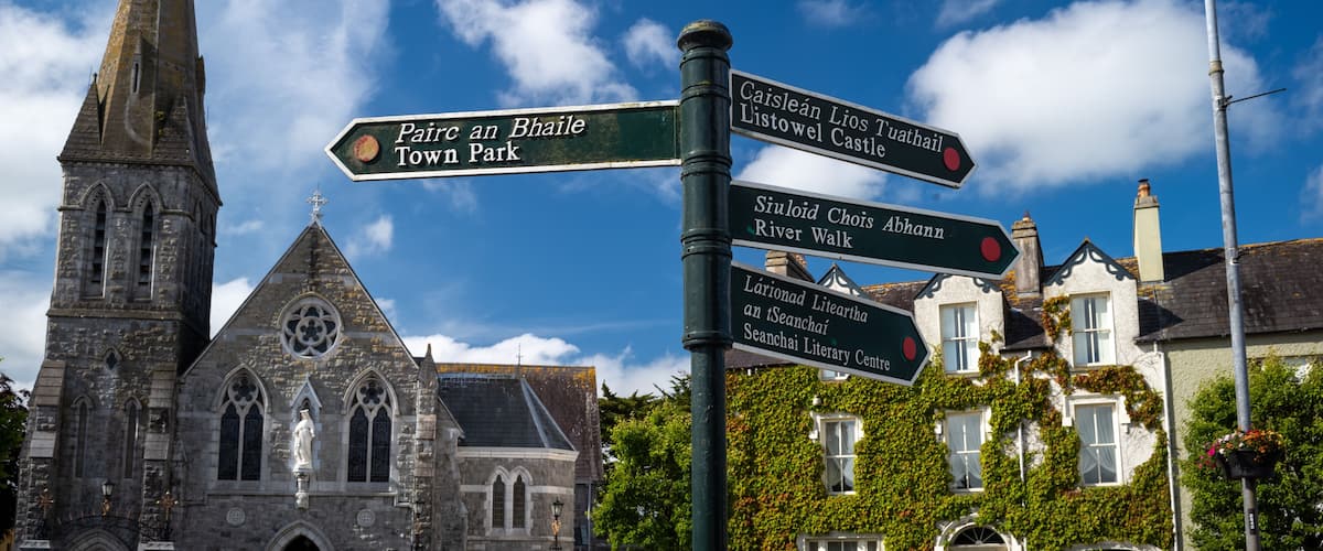A church with a pointed steeple, a signpost with directions to various local attractions, and a clear blue sky with scattered clouds.