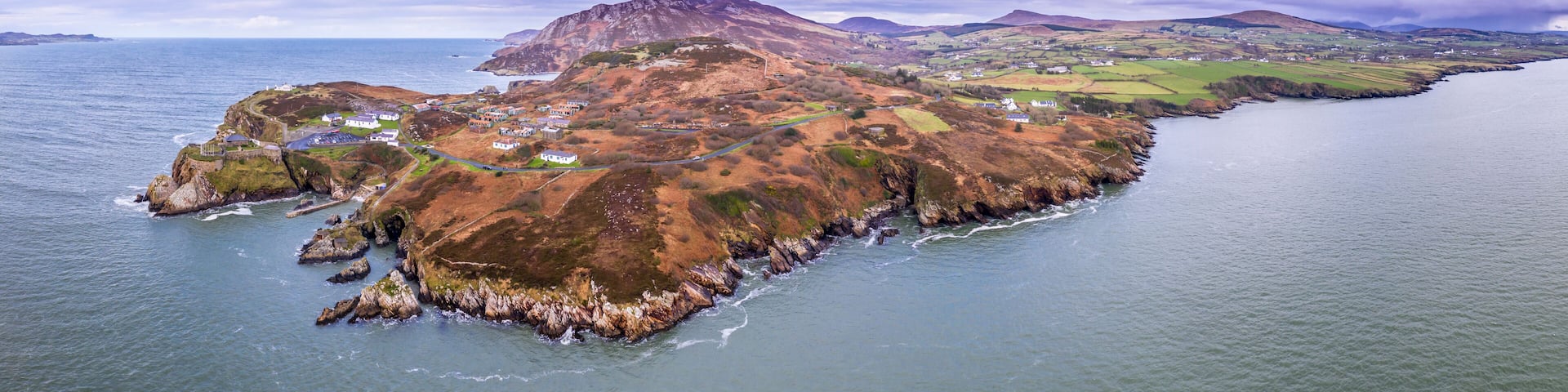 A coastal landscape with rocky cliffs, a winding road, and scattered houses.