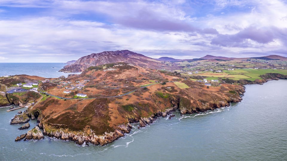 A coastal landscape with rocky cliffs, a winding road, and scattered houses.