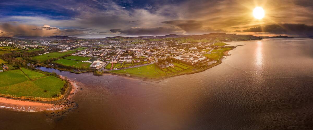 An aerial view of a coastal town with a river, green fields, and a large body of water.