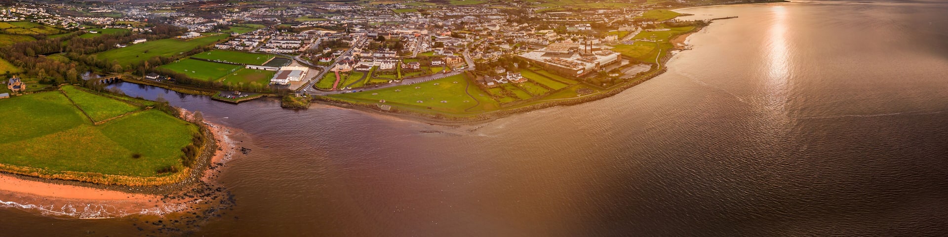 An aerial view of a coastal town with a river, green fields, and a large body of water.
