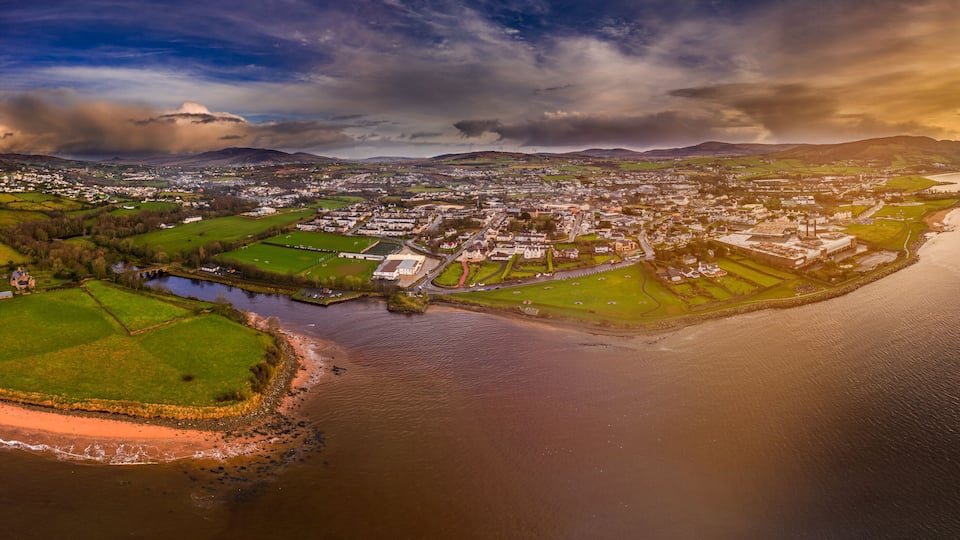 An aerial view of a coastal town with a river, green fields, and a large body of water.