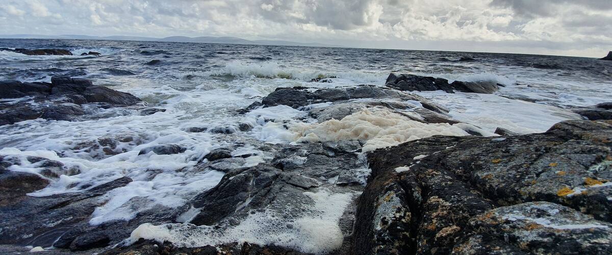 A rocky shoreline with turbulent waves and a cloudy sky.