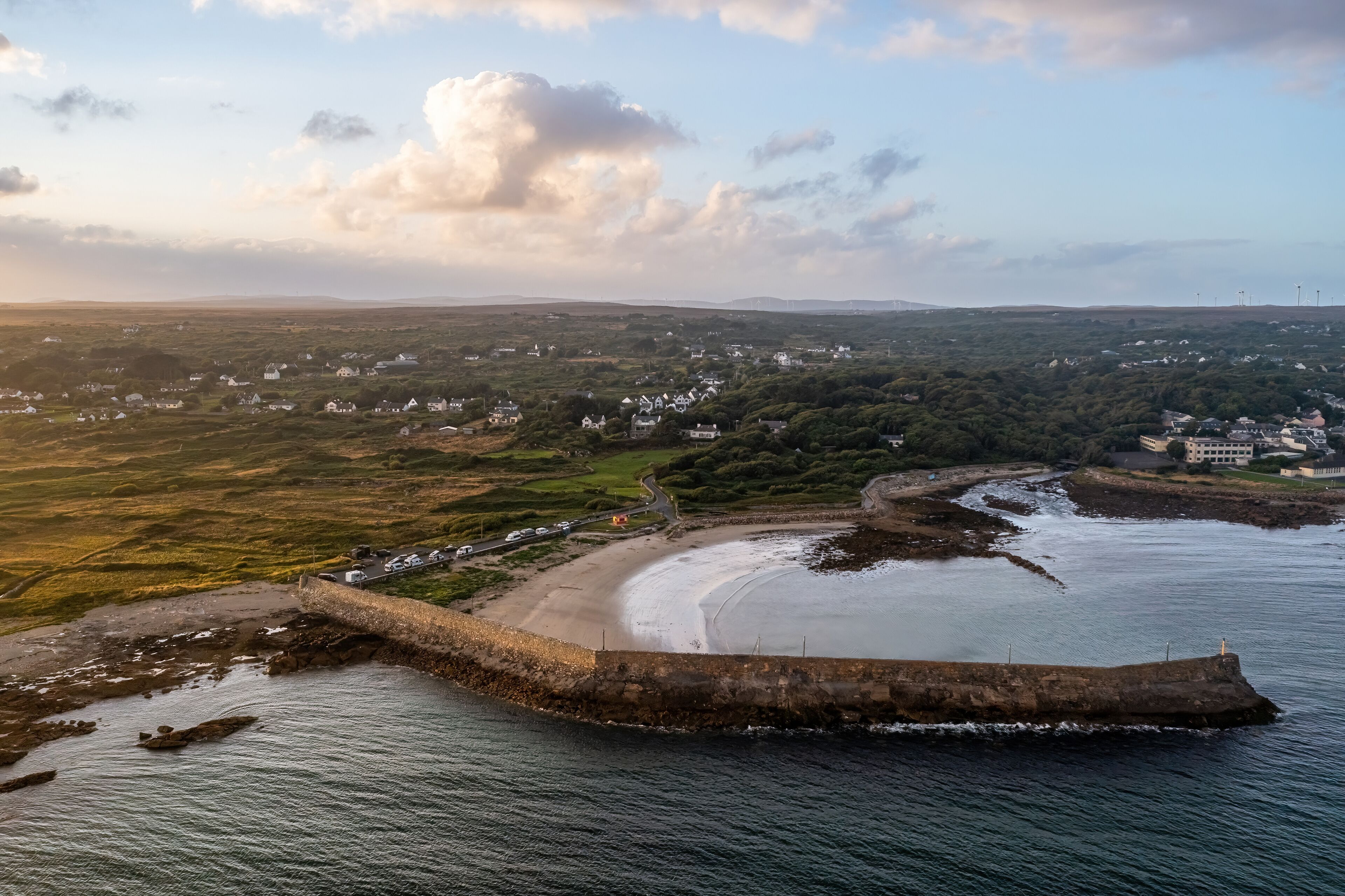 Aerial photograph of Spiddal Pier at sunset, featuring camper vans parked on the beach with the river flowing into the sea in the background