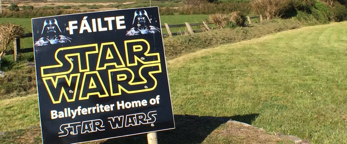 Un letrero con temática de Star Wars, situado en una zona cubierta de hierba con vistas a montañas y al océano al fondo.
