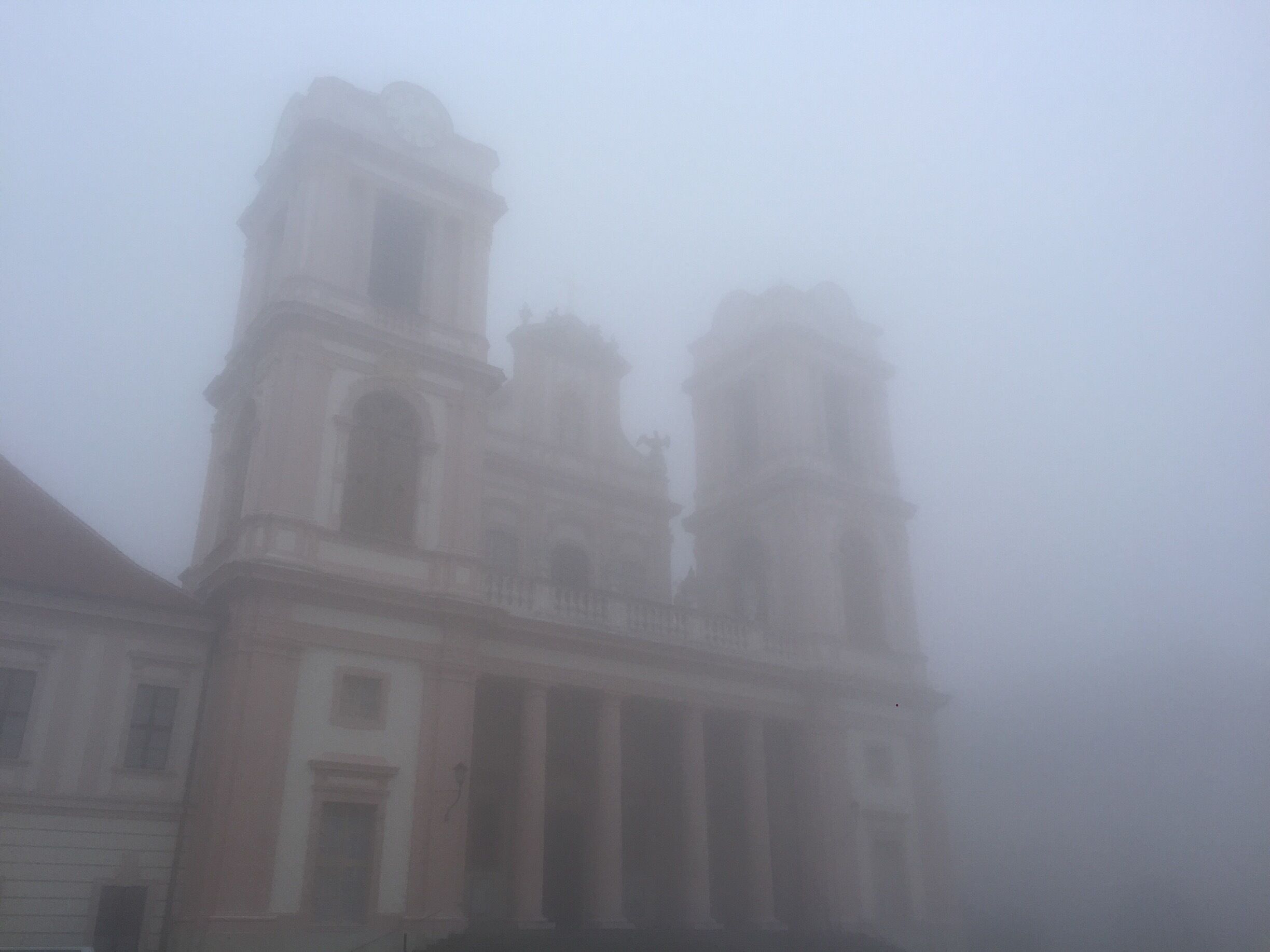 A foggy view of a historic building with a bell tower and classical architecture.