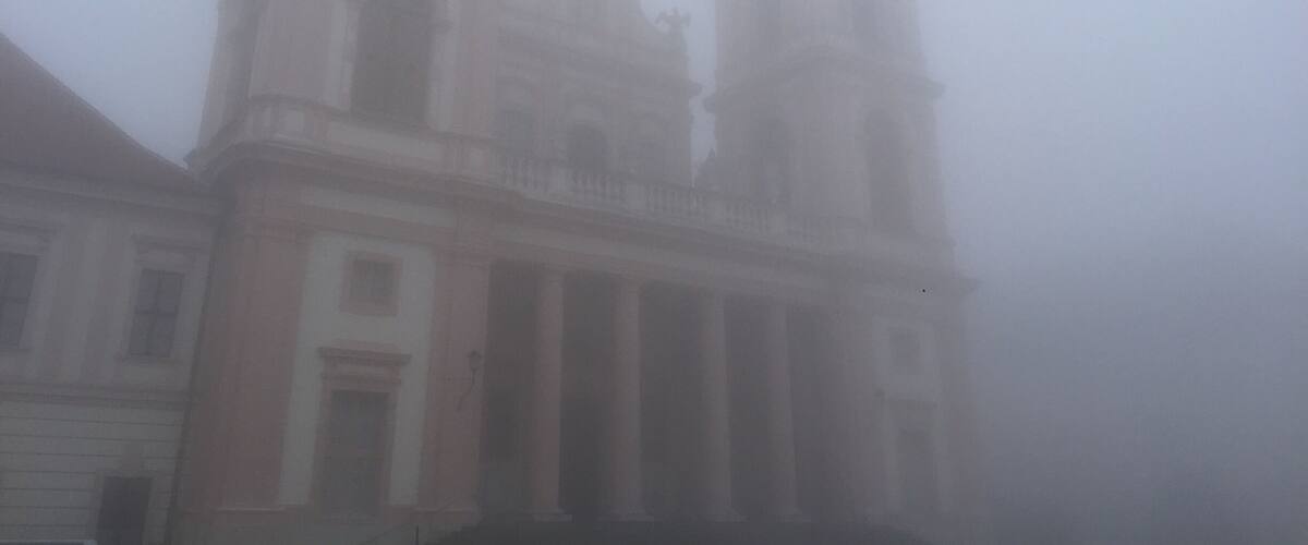 A foggy view of a historic building with a bell tower and classical architecture.