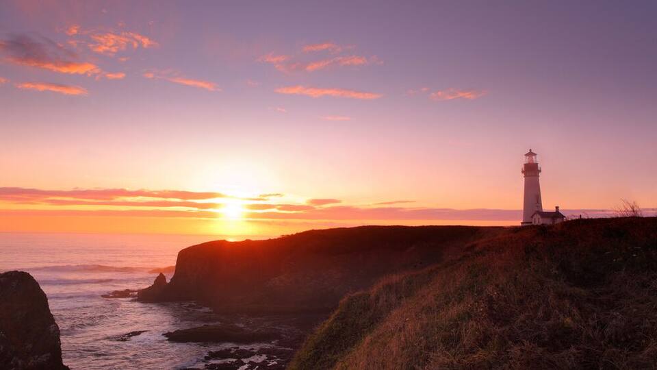 Un atardecer costero con un faro en un acantilado.