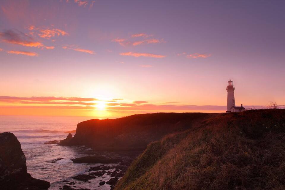 A coastal sunset with a lighthouse on a cliff.