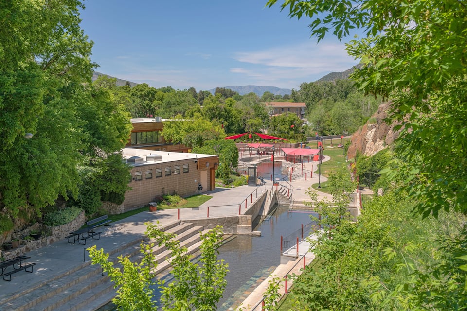 Un parque con un elemento acuático, edificios con tejados rojos y un inmueble con fachada de vidrio.