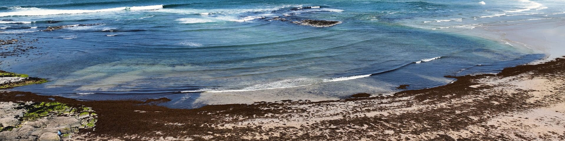 A coastal landscape with waves, a sandy beach, and distant hills.