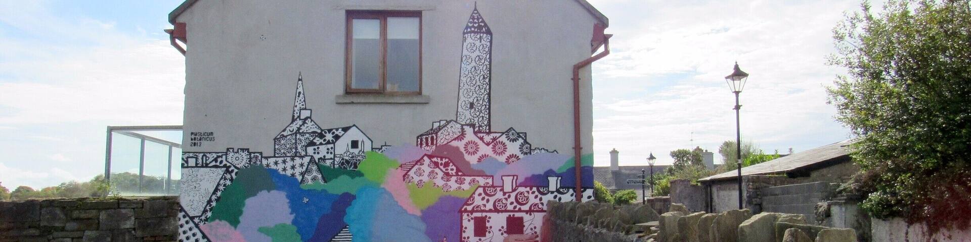 We were passing through Killala and saw a Round Tower (the Killala Round Tower), while walking around to get a better view of the Tower we spotted this mural on the side of a Home.