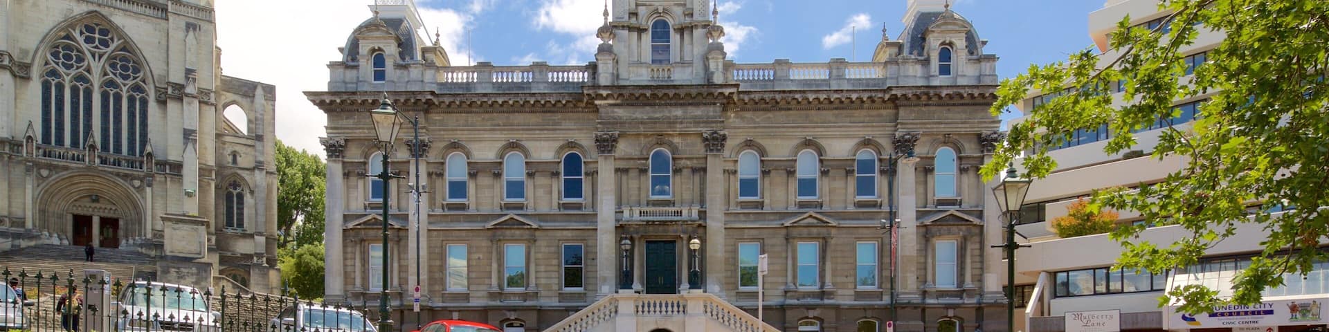 A historic building with a clock tower, surrounded by modern buildings and a clear blue sky.