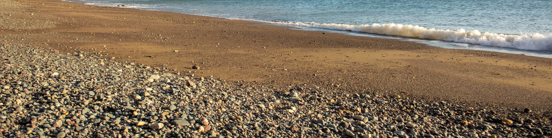 A pebbly beach with a rocky cliff and calm sea.