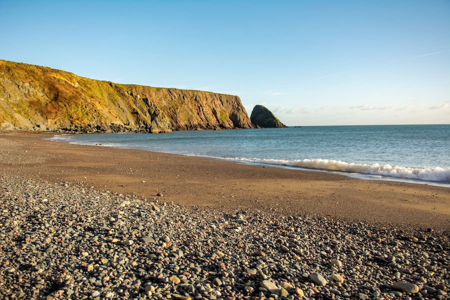 A pebbly beach with a rocky cliff and calm sea.