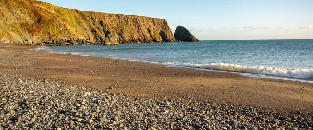 A pebbly beach with a rocky cliff and calm sea.