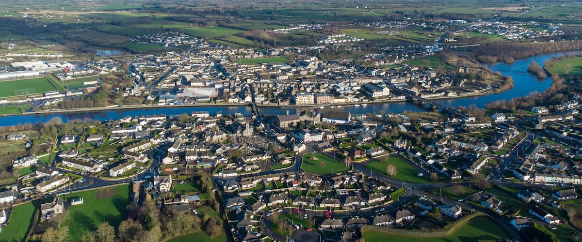 An aerial view of a town with a river running through it, surrounded by green fields and hills.