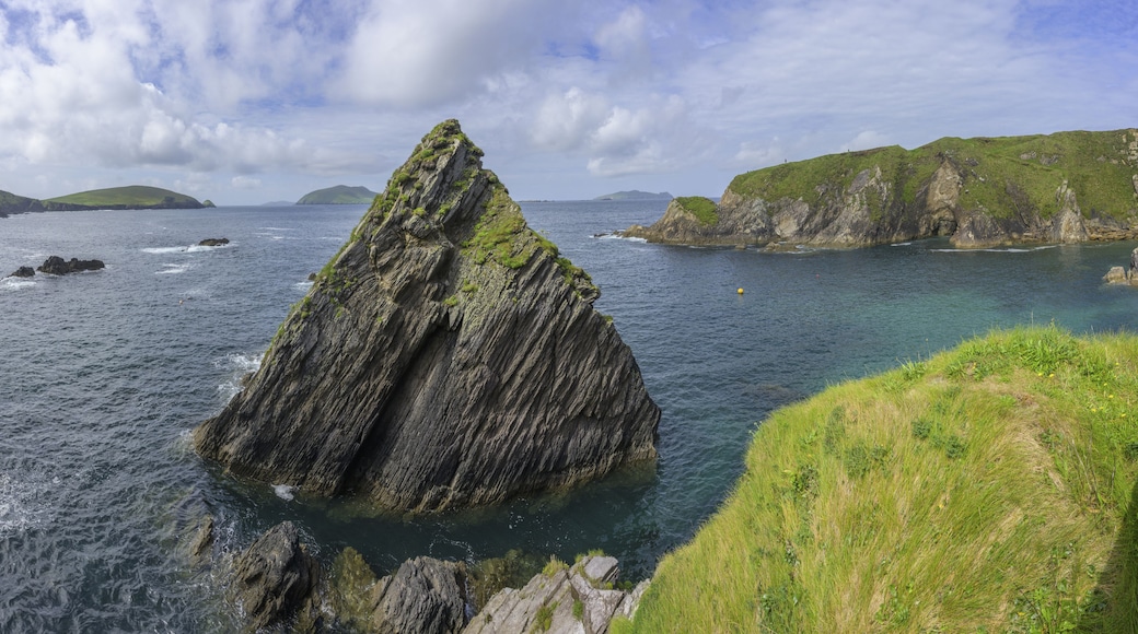 A rugged coastline with a prominent rock formation surrounded by calm sea and grassy hills.