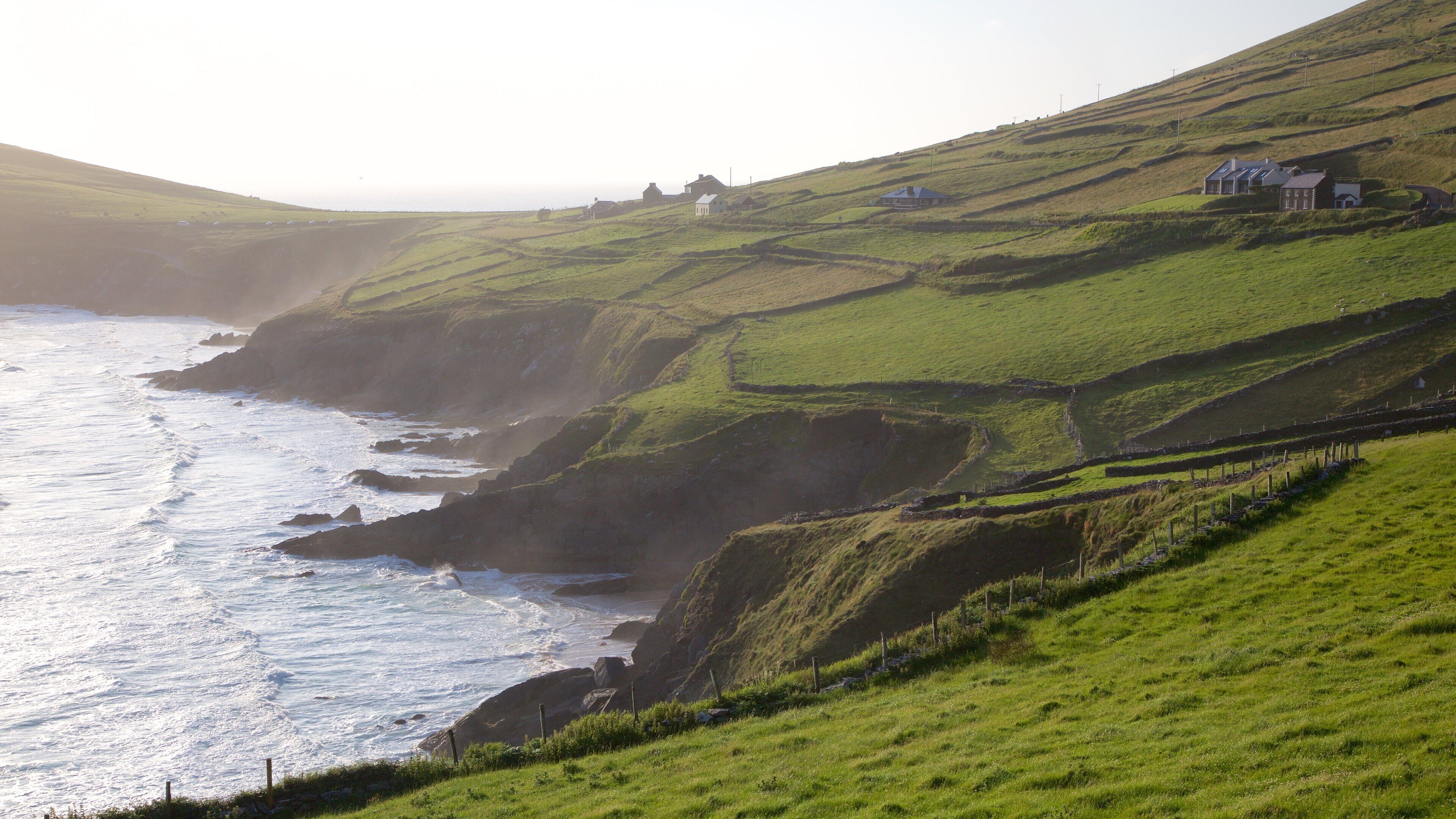 A coastal landscape with rolling hills, a rocky coastline, and a few houses.