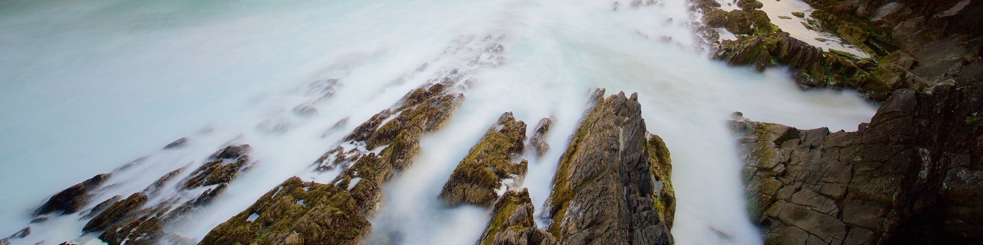 A coastal landscape with rocky cliffs, a calm sea, and a clear sky.