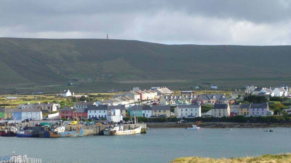 A coastal town with colorful houses, a harbor with boats, and a hill in the background.