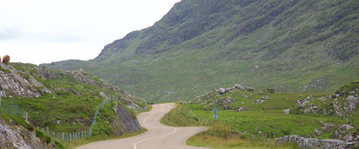 A winding mountain road with rocky terrain and grassy areas.