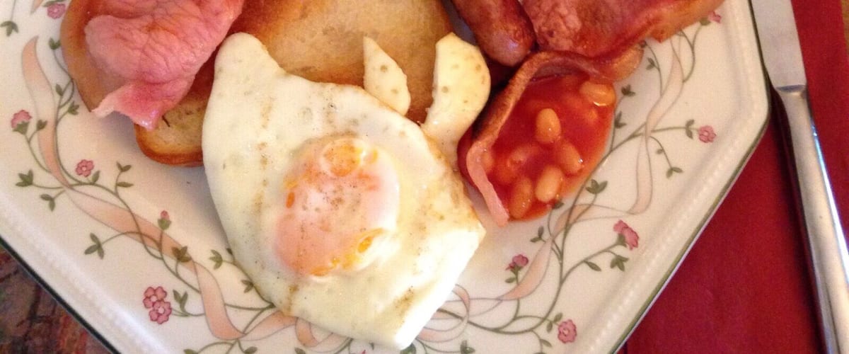 A plate of breakfast food including bacon, sausages, a fried egg, and beans.