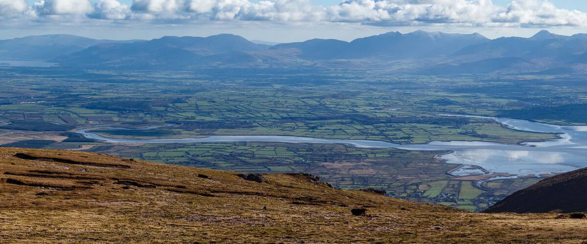 A mountainous landscape with a river winding through fields and valleys.