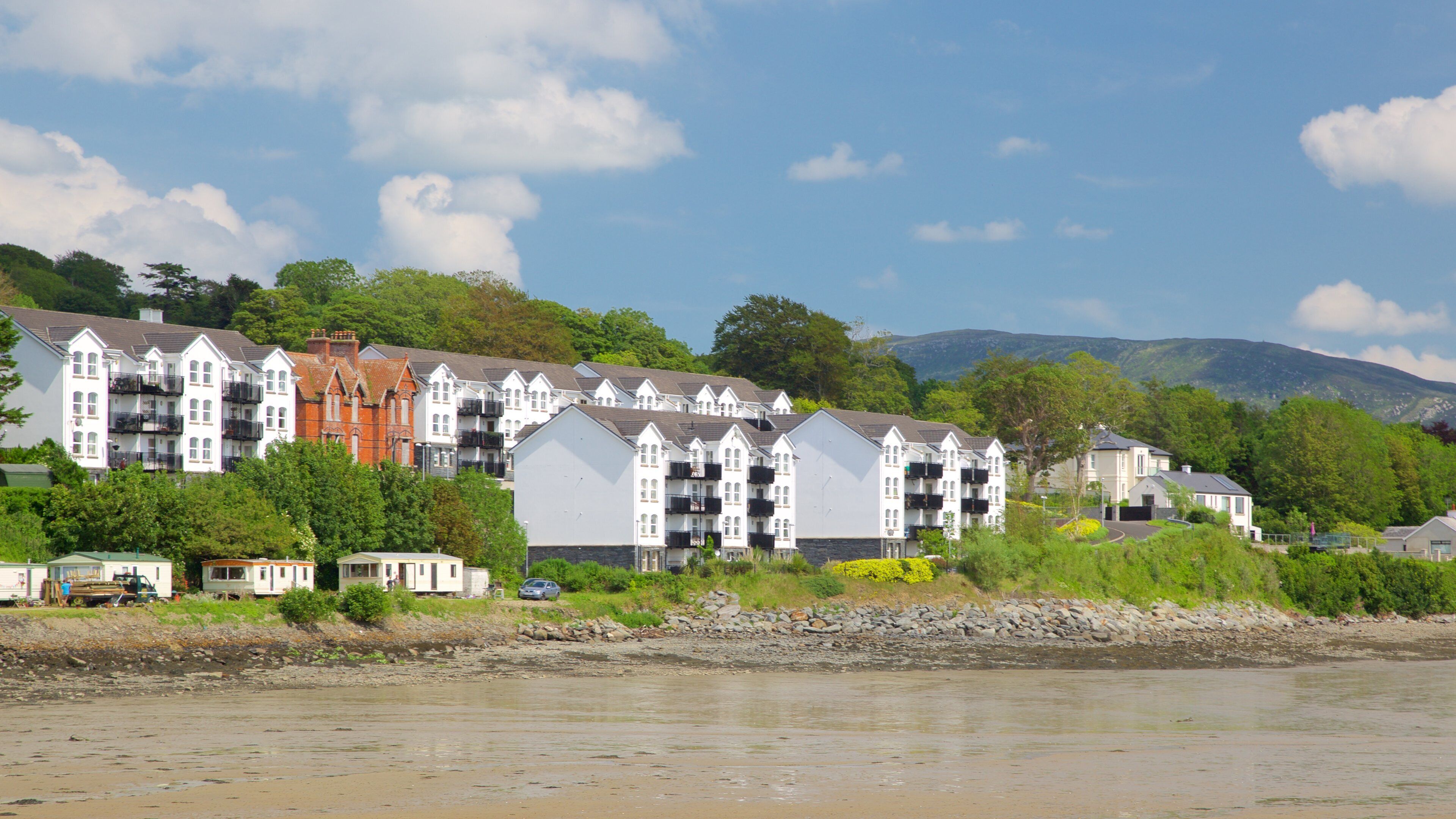 A coastal residential area with multi-story buildings, a rocky shoreline, and a backdrop of hills and trees.