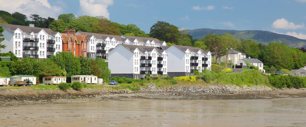 A coastal residential area with multi-story buildings, a rocky shoreline, and a backdrop of hills and trees.