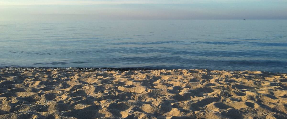A sandy beach with a calm sea and a clear sky.