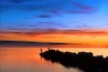 A sunset over a calm body of water with rocky outcrops and silhouettes of people fishing.