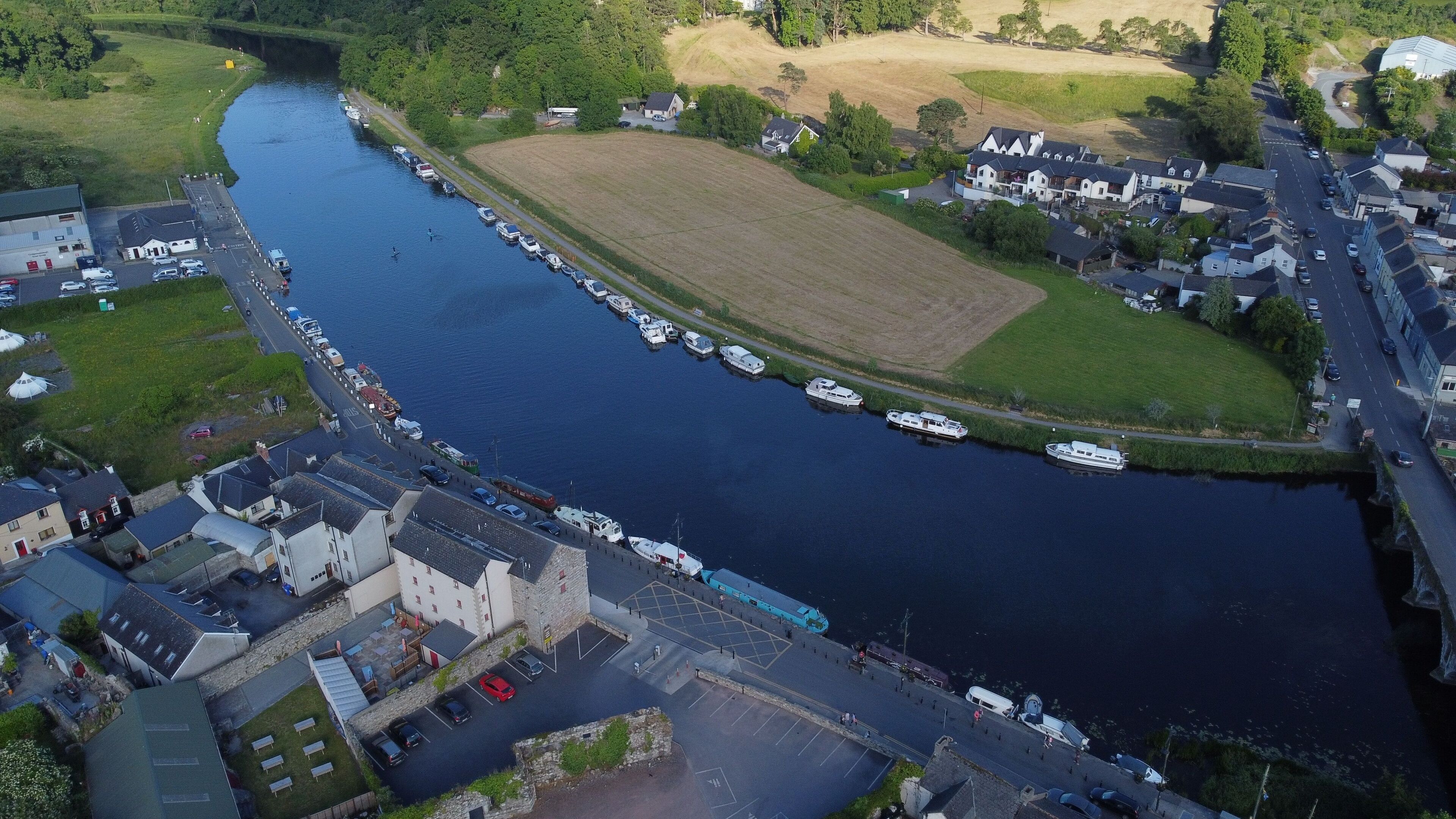 A river with boats docked along the banks, surrounded by residential buildings and a large open field.
