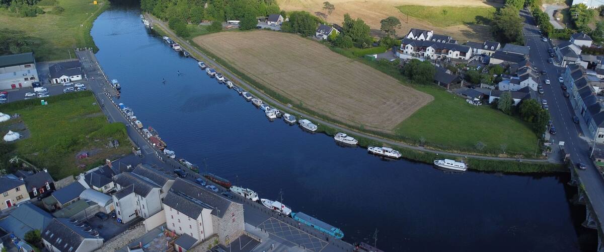 A river with boats docked along the banks, surrounded by residential buildings and a large open field.