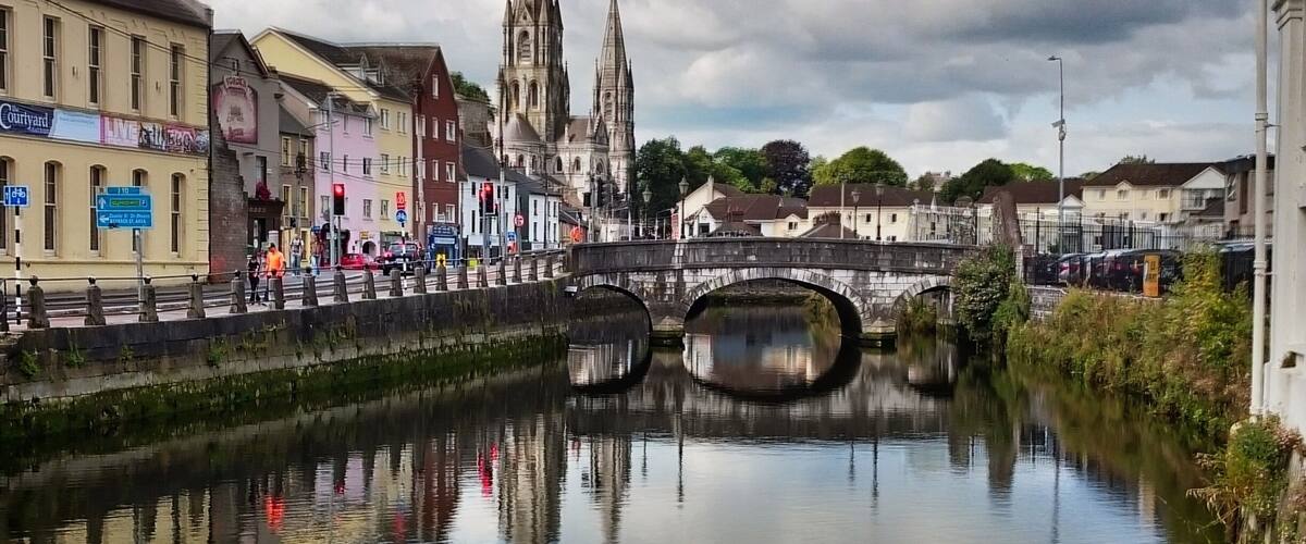 A river with a stone bridge, a cathedral, and colorful buildings along the riverbank.
