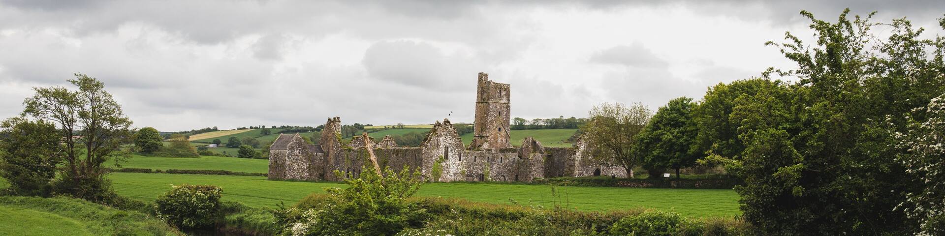 A historic stone castle surrounded by lush green fields and a small stream.
