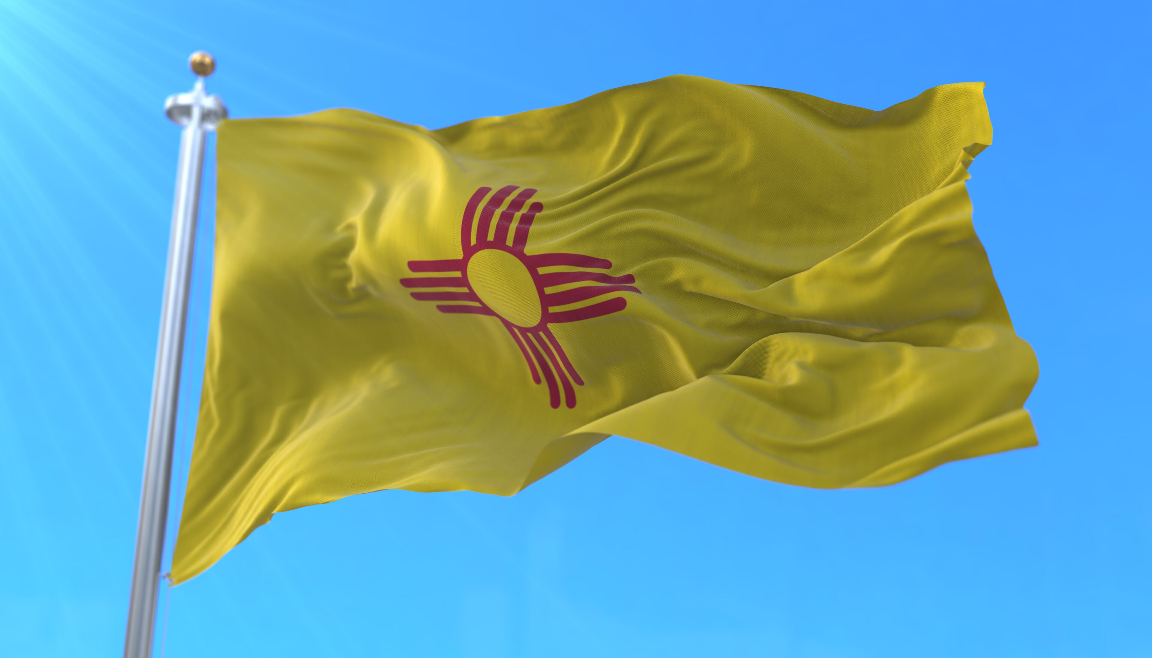 A yellow flag with a red sun and rays on a flagpole against a clear blue sky.