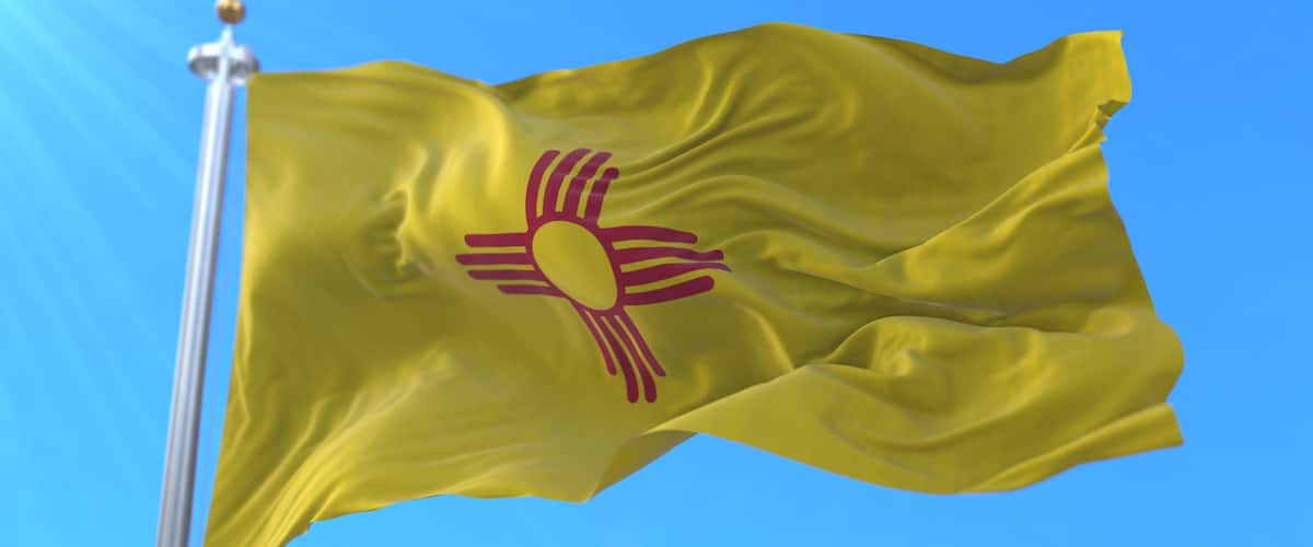 A yellow flag with a red sun and rays on a flagpole against a clear blue sky.