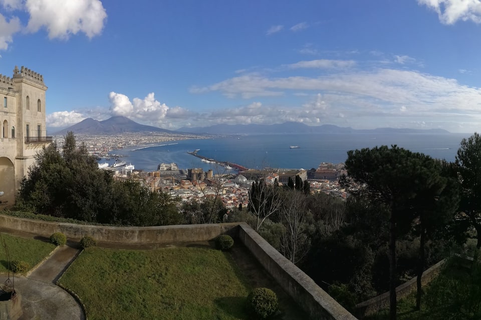 Un paysage urbain côtier avec un bâtiment imposant, une montagne et un ciel bleu dégagé.