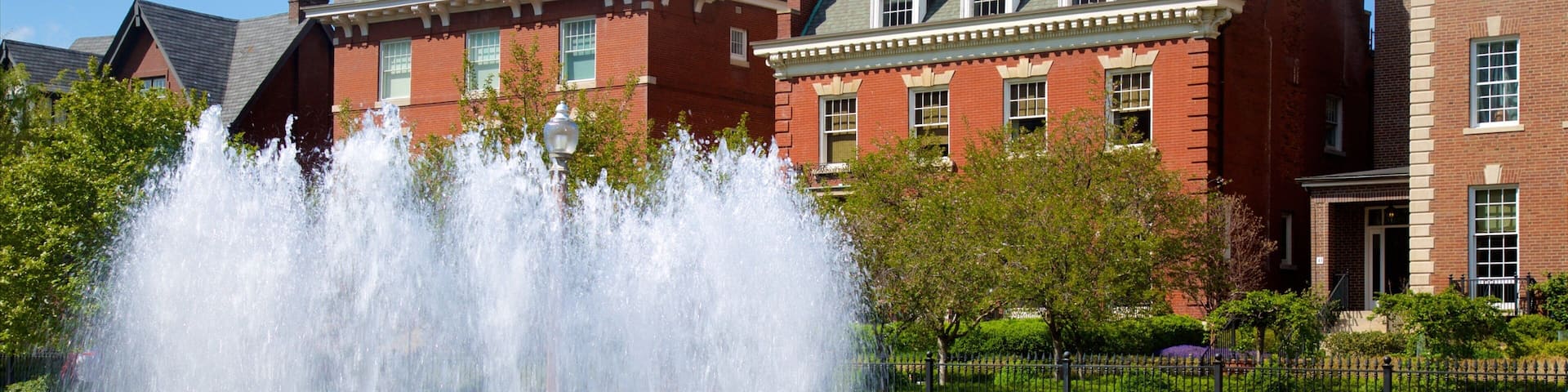A fountain in front of a red brick building with green roofs and white trim.