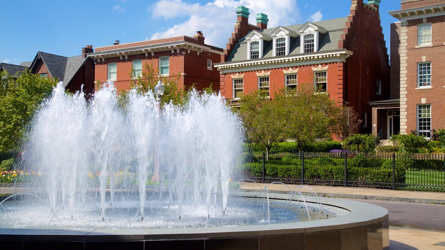 A fountain in front of a red brick building with green roofs and white trim.