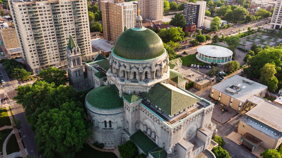 Un bâtiment historique surmonté d’un dôme vert, entouré de gratte-ciel modernes.