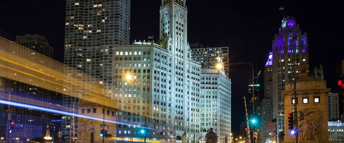 A nighttime cityscape with illuminated skyscrapers and a prominent clock tower.