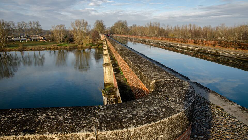 A canal with a brick wall and calm water reflecting the sky.