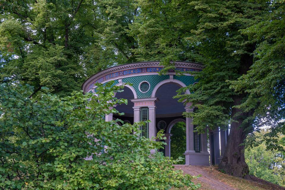 A historic building with a green and blue facade, surrounded by lush trees.