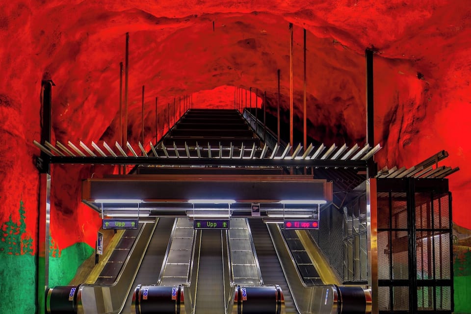 An underground station with escalators and a red-lit tunnel.