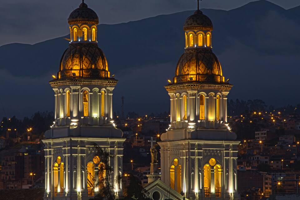 Two illuminated church domes with cross-topped spires, set against a mountainous backdrop.