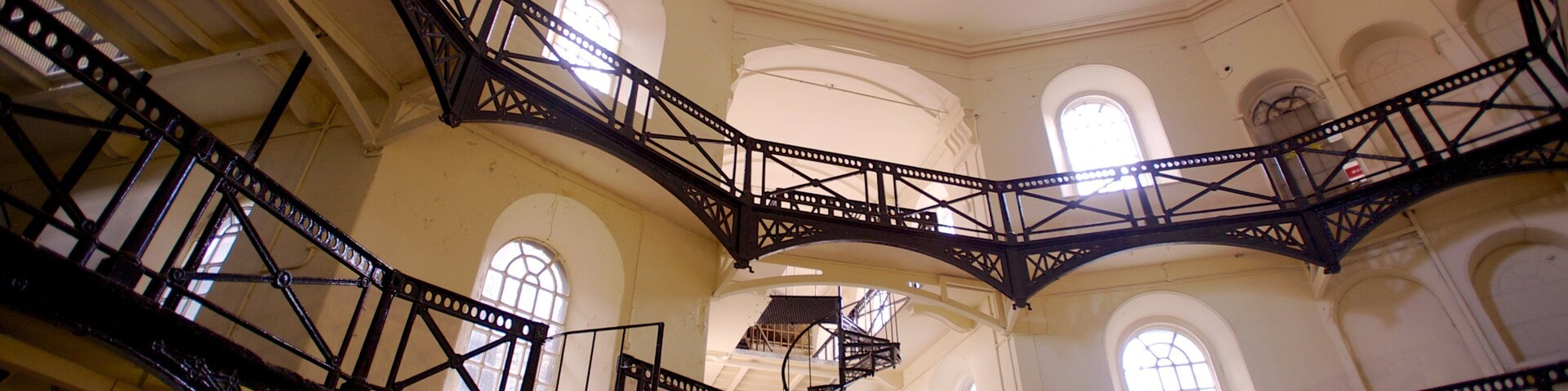 Un escalier en fer à plusieurs niveaux, agrémenté d’arches et de fenêtres, dans un bâtiment.